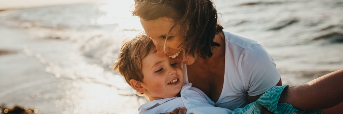 Mother and child sharing a playful moment on the beach at sunset.