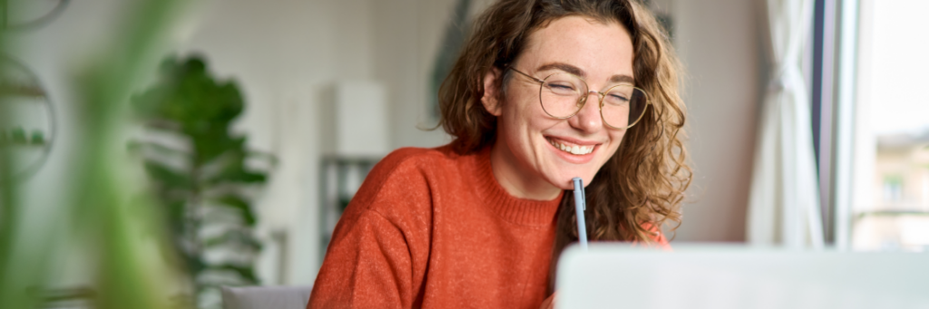 Woman smiling while looking at computer screen in a well-lit room.