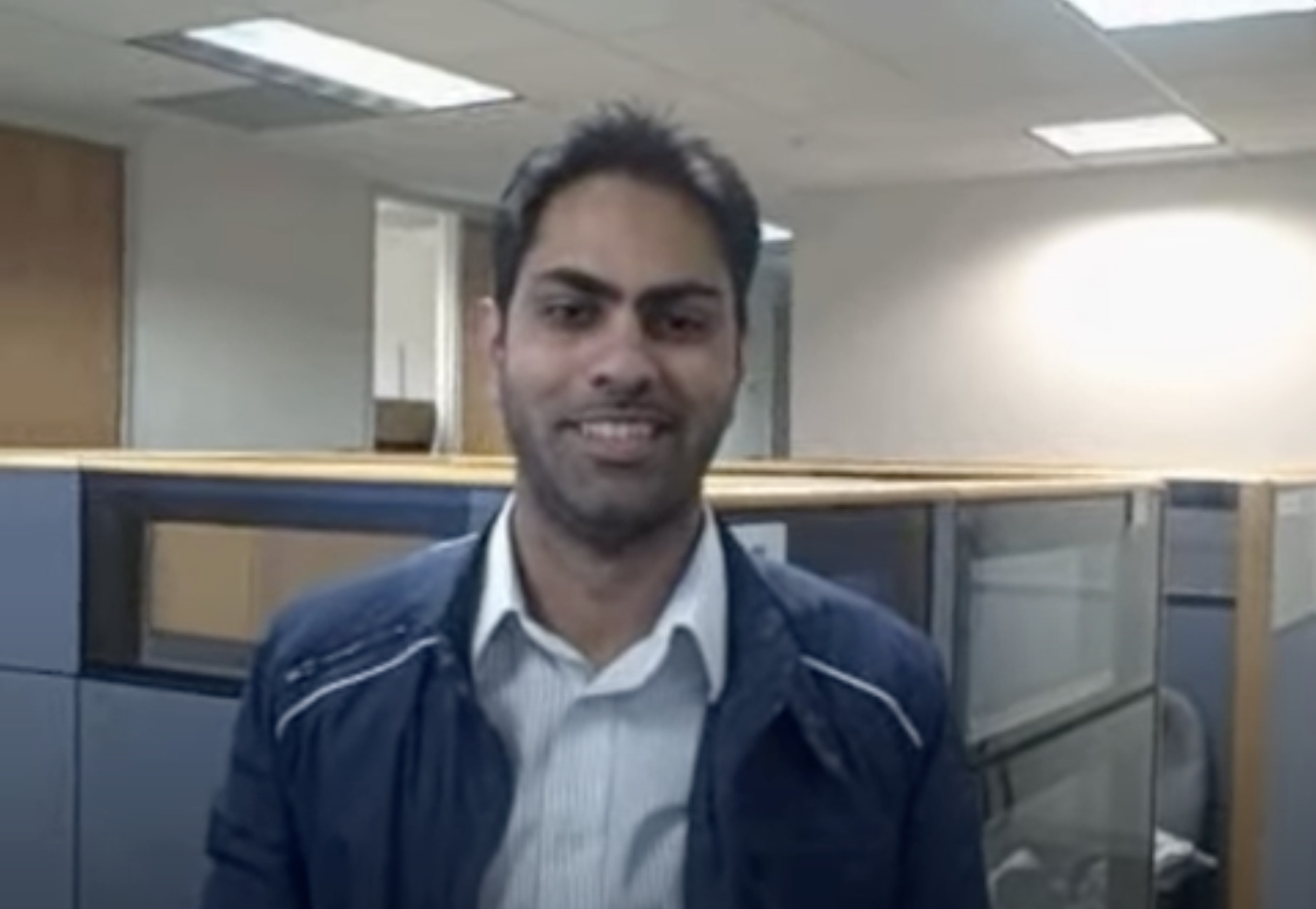 Man in a leather jacket smiling at the camera in an office cubicle setting, working on Biteable video maker.