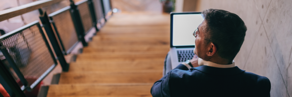 Man in a suit working on a laptop while seated on steps.