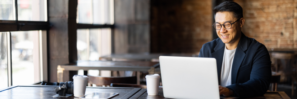 Smiling person creating content with Biteable video maker on a laptop in a cozy cafe setting.