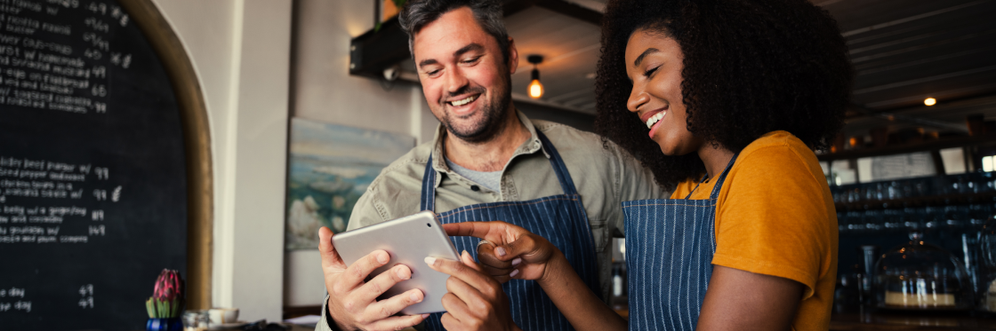 25 business video ideas for inspiration Two baristas smiling and looking at a Biteable video maker tutorial on a tablet in a cafe.