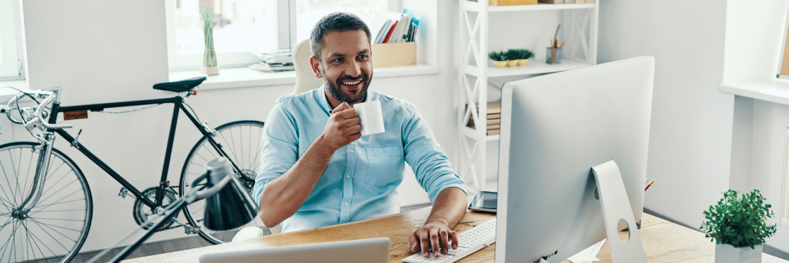 Website makers best website builders for making a gorgeous website Man with a coffee mug smiling while working at a computer in a bright office setting.