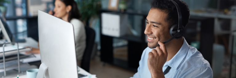 Man with headset smiling and looking at computer screen in office setting, using Biteable video maker.