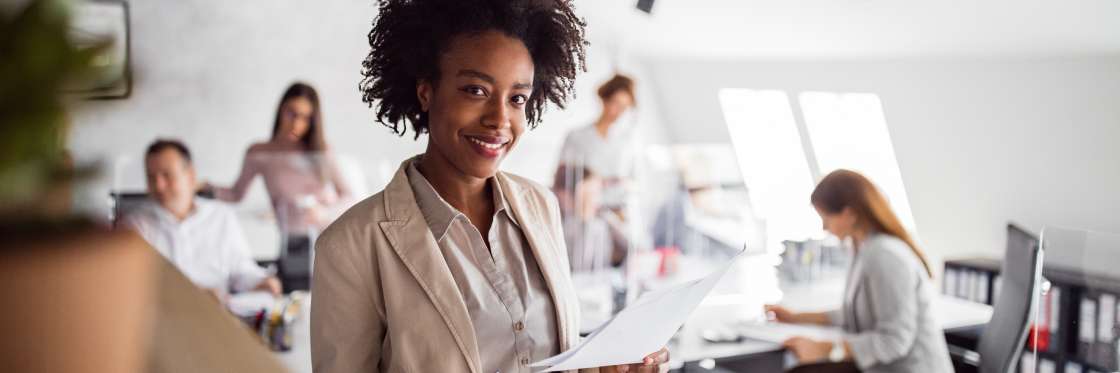 Confident businesswoman holding documents with colleagues working in the background, featured in a Biteable video maker presentation.