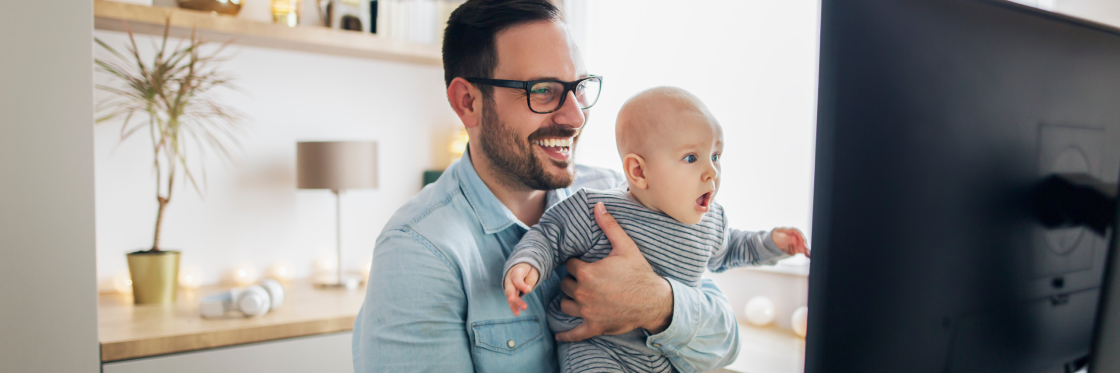 Employee engagement ideas for your remote team Man holding a baby while working on a computer at home.