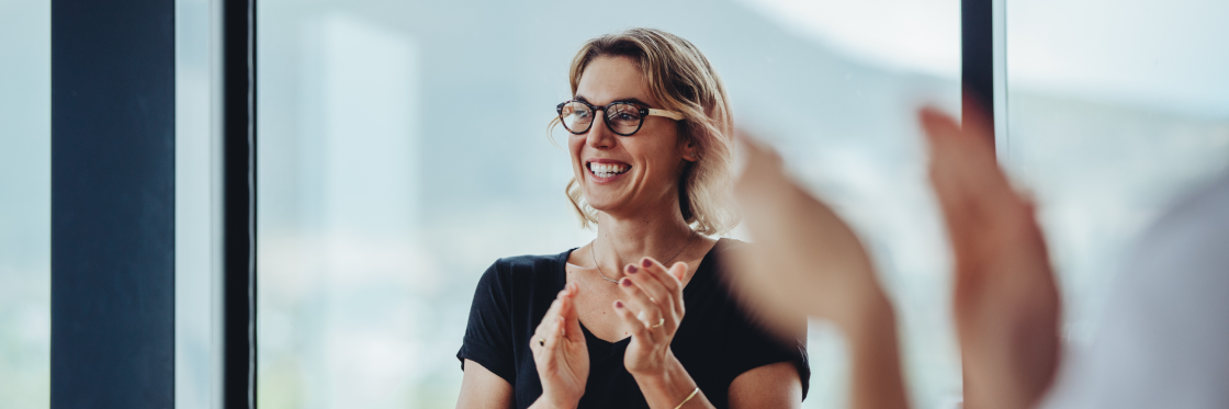 Woman smiling and clapping her hands during a meeting focused on employee recognition ideas.