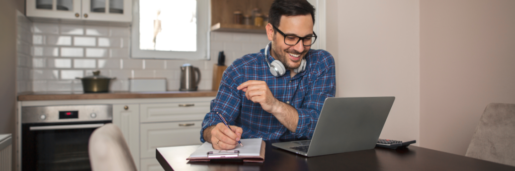 Man with headphones working on a laptop and writing notes in a home kitchen using Biteable video maker.