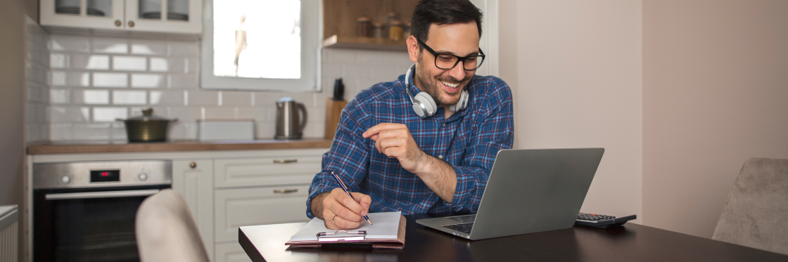 Man with headphones working on a laptop and writing notes in a home kitchen using Biteable video maker.