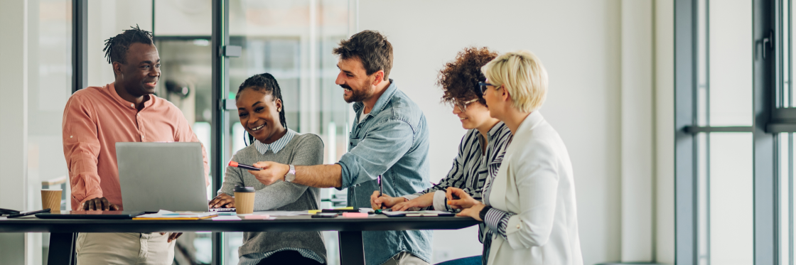 6 ways to improve sales team performance Diverse team of professionals engaged in a collaborative discussion around a laptop in a modern office setting.