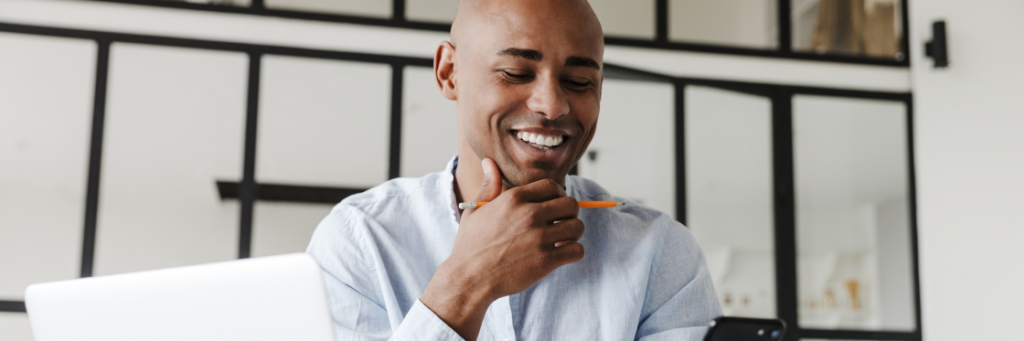 A smiling person looking at a smartphone with a laptop open in front of them.