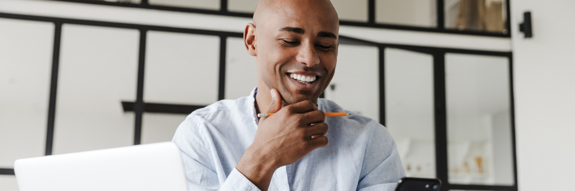 A smiling person looking at a smartphone with a laptop open in front of them.