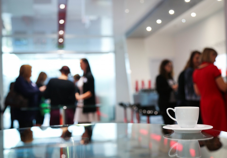 Group of people networking in a modern conference room with a focus on a coffee cup in the foreground.