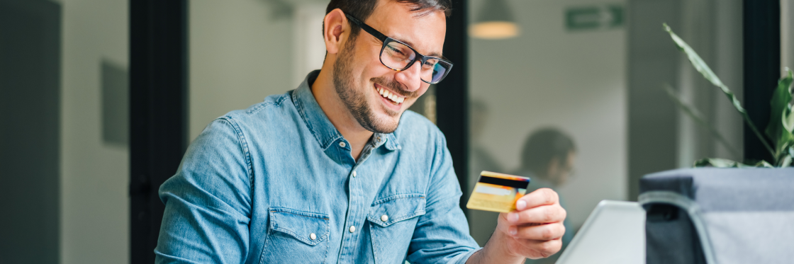 How Fattmerchant saved 36% on leads with a Biteable video Man smiling while looking at a credit card and using a laptop.