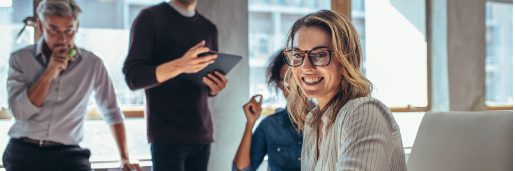 Colleagues in a casual office setting with one woman smiling at the camera.