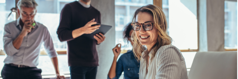 Colleagues in a casual office setting with one woman smiling at the camera.