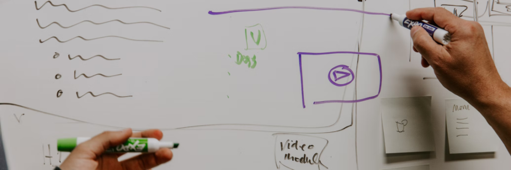 A person using a blue marker to draw on a whiteboard in a brainstorming session.