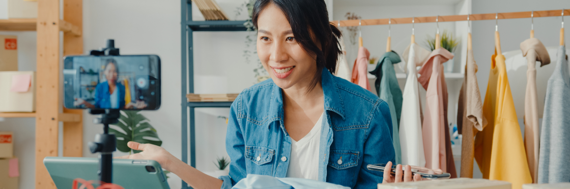 Start a YouTube Channel Woman recording a fashion vlog on her smartphone in a studio with clothes in the background.