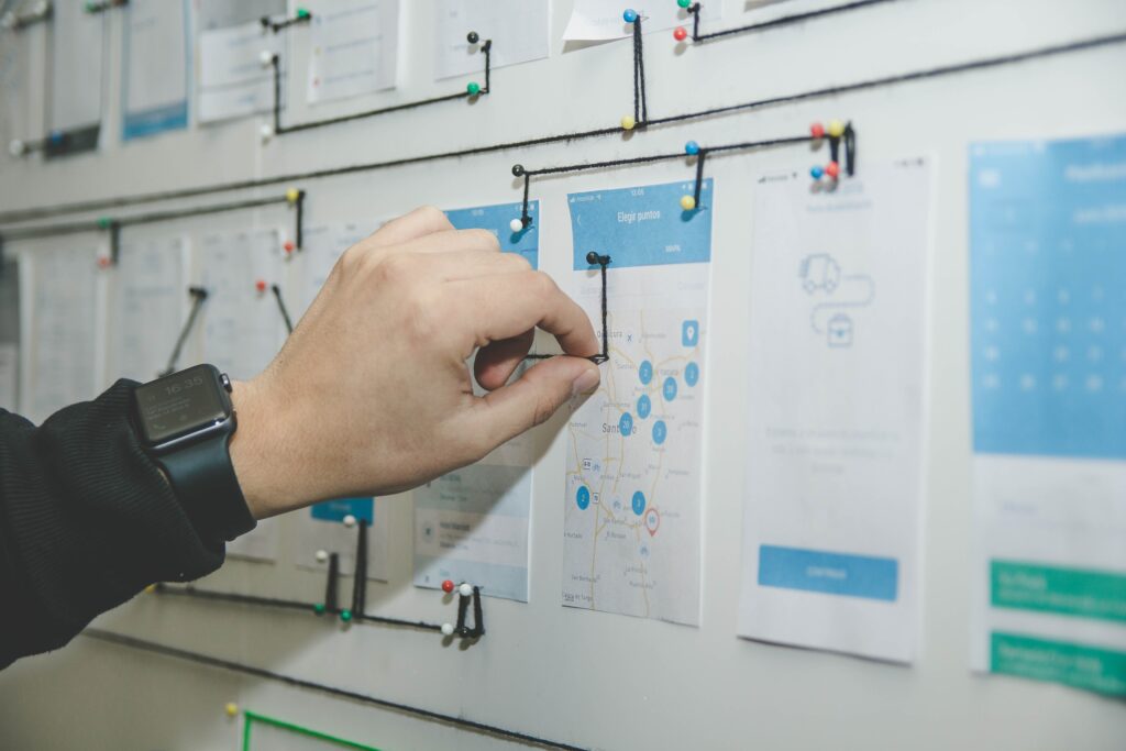 Person pinning a document on a bulletin board with various other charts, notes, and a Biteable video maker tutorial printout.