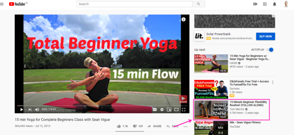 A screenshot of a youtube video titled "15 min yoga for complete beginners with sean vigue," showing a man demonstrating a yoga pose on a mat outdoors.