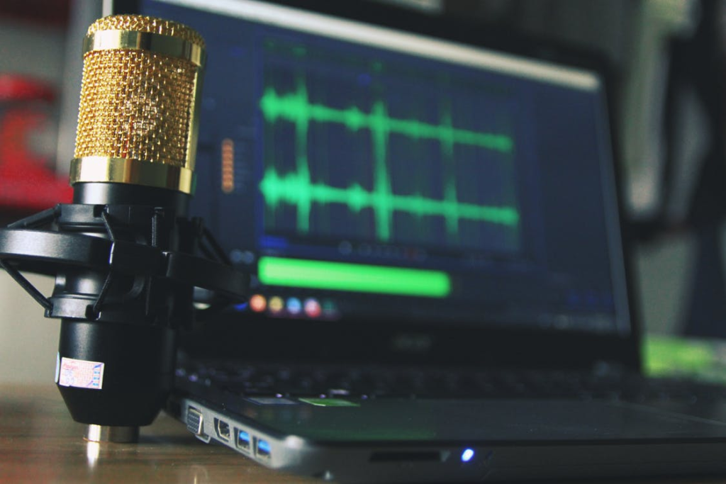 Condenser microphone in the foreground with a laptop displaying audio recording software in the background.