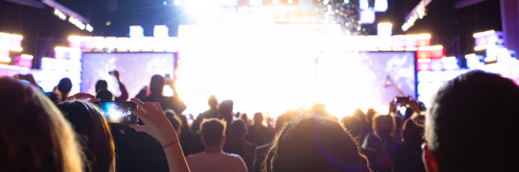 Crowd of spectators with raised smartphones capturing a brightly lit stage event.