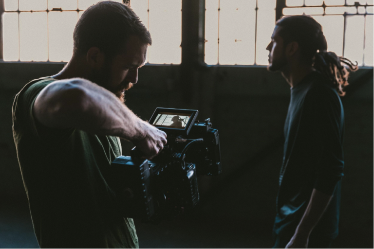 Two men reviewing footage on a camera screen in a dimly lit room.