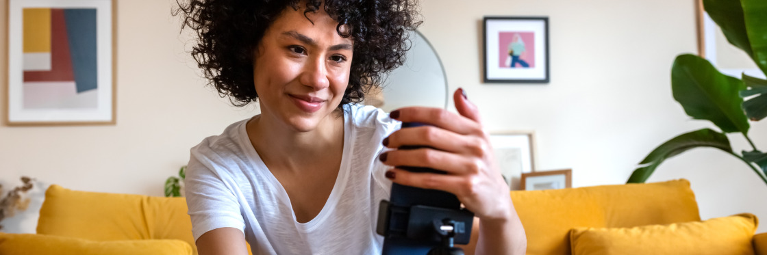 YouTube Shorts Boosting your business with short-form videos Woman with curly hair smiles while taking a photo with a camera in a cozy living room setting using Biteable video maker.