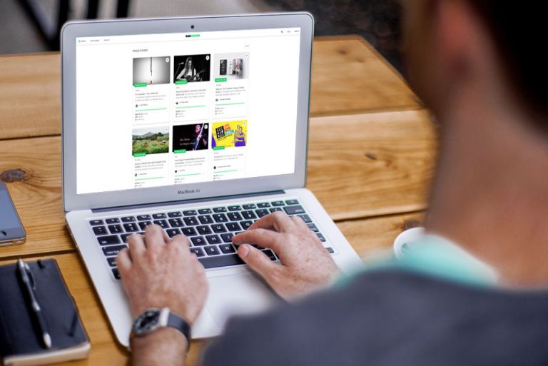 Man browsing the Biteable video maker website with various thumbnails on a Macbook laptop at an outdoor wooden table.