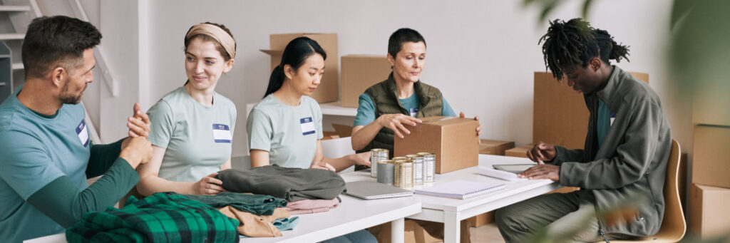 A diverse group of volunteers packaging food donations in a bright room, wearing casual clothing and name tags, actively engaging in conversation for a Biteable video maker project.