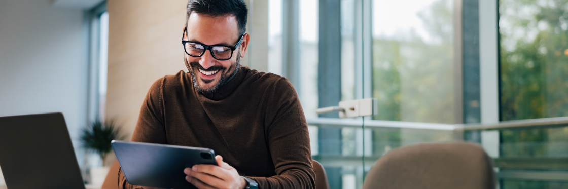 A man with glasses, smiling while looking at a digital tablet in a modern office setting, using Biteable video maker.