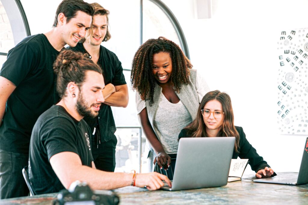 Five colleagues collaborate around a laptop in a bright office, displaying engagement and teamwork, aiming to motivate Gen Z.