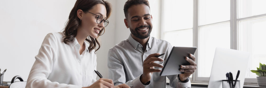 Two professionals, a woman and a man, collaborating over a digital tablet in a bright office space.