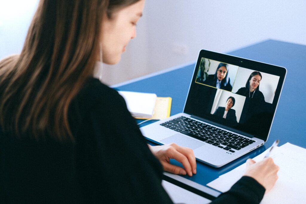 A woman participates in a video call with three colleagues on her laptop in an office setting.