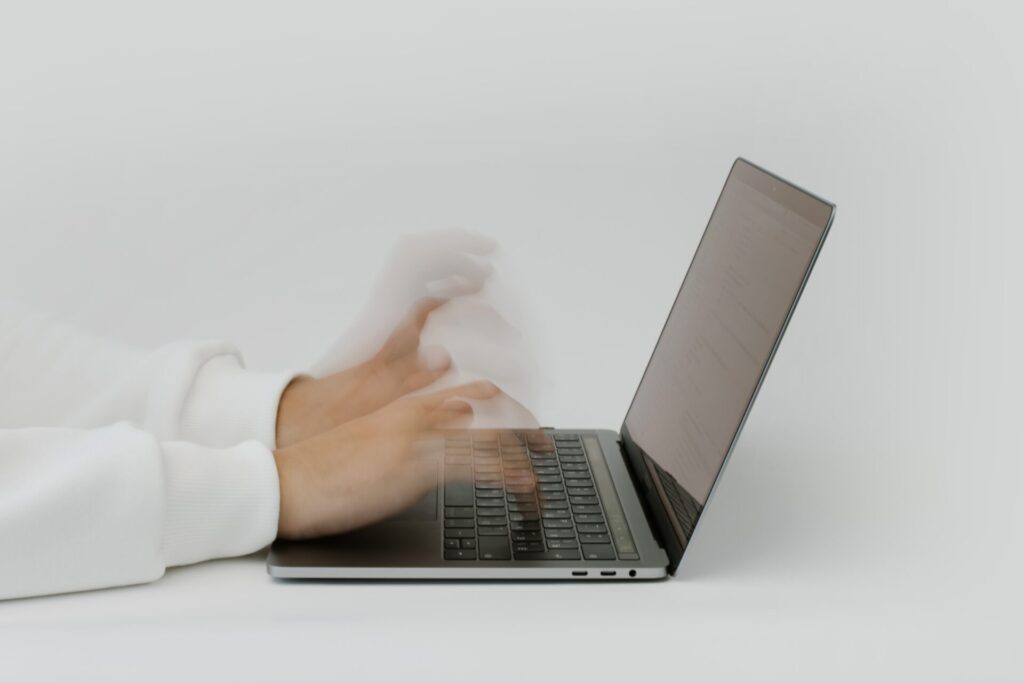 A person in a white sleeve typing on a laptop, with their hands appearing blurred due to rapid movement, against a white background.