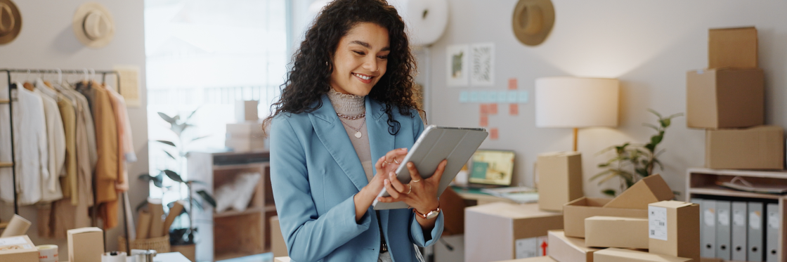 How to master marketing as a solopreneur A woman smiles while using a tablet in a creative office space with boxes and fashion items in the background. Biteable video maker