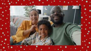 A smiling family of three sits on a couch, taking a selfie in a brightly lit living room, with a red, polka-dotted border around the image.