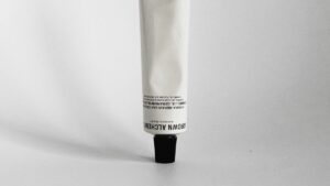 A white tube with a black cap is positioned upside down against a plain, light background. The label contains text in black.